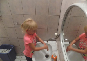 Klara ćwiczy prawidłowe mycie rąk przy umywalce.